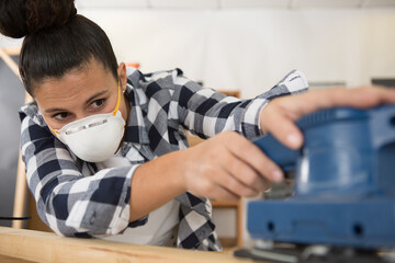 middle aged professional female carpenter sanding in workshop