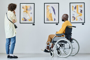 Rear view of young woman and man with disability watching pictures at art gallery