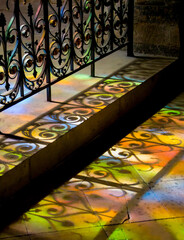 Reflets de lumières des vitraux d'une église sur le sol en pierre et une grille en fer forgé (detail)