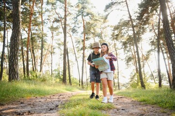 Happy excited school children with backpacks in casual clothes enjoying walk in forest on sunny autumn day, two active kids boy and girl running and playing together during camping trip in nature.