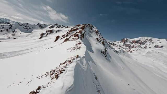 Aerial view flight climbing mountain summit cliff texture snow reversal dive from top ridge alpine sunny landscape. FPV sports drone epic rock scenery skyline panorama wild hilly valley freeze glacier