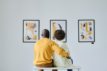 Rear view of multiethnic couple embracing while sitting at art gallery, they enjoying modern art