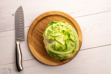 One fresh juicy organic cabbage on a round wooden tray with a metal knife, close-up, on a wooden table, top view.