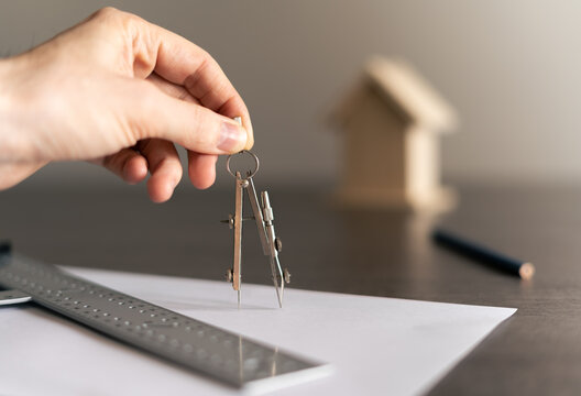 Architect drawing with the compass on a white paper the plans of a new home for a family.