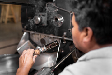 An Hispanic man is checking the roast of the beans from the coffee roaster machine