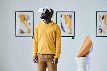 African young man using VR glasses while visiting art gallery