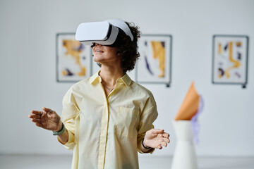 Young girl standing and gesturing in virtual reality glasses visiting virtual art gallery