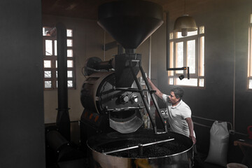 Fototapeta na wymiar A Hispanic man is operating the lever of a coffee roaster machine