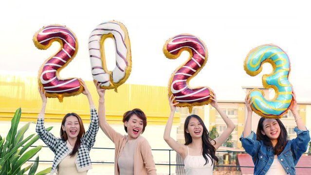Happy new year 2023, young Asian woman raising number balloon symbol on rooftop outdoor at sunset