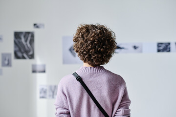Rear view of young woman with curly hair visiting photo gallery, she enjoying modern art
