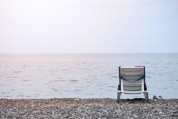 Chair on bank of pebbles with the sea and beach