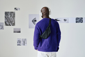 Rear view of African young man in wireless headphones listening to guide and watching photos on the...