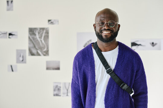 Portrait of African young man in eyeglasses smiling at camera standing at art gallery
