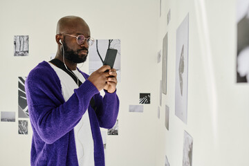 African man in headphones using smartphone while visiting art gallery
