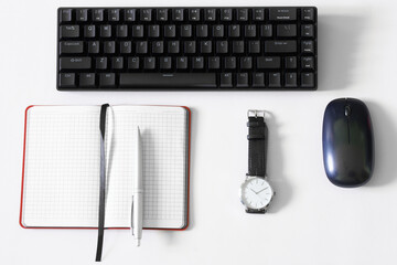 Portable wireless mechanical computer keyboard on a white background next to a wristwatch, an open notepad, a computer mouse and a fountain pen. Modern gadgets for work and gaming