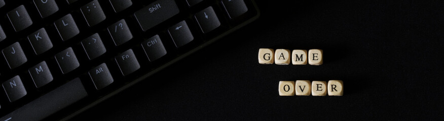 Game over inscription on a black background next to a black mechanical keyboard. Fate, destiny, gambling addiction and the predetermination of the finale. Tragedy and pessimism. Web banner.