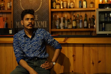 man wearing blue shirt sitting infront of bar