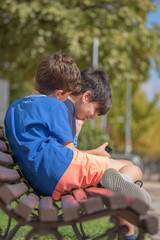 side view of kids playing enjoying smart phone videos and games sitting on a park bench