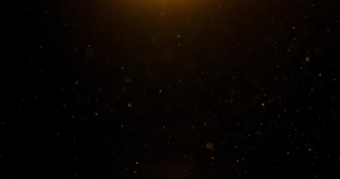 Gold particles flying in wind on black background, depth of field. Golden glitter slow motion in spot light. Dust particles 4k overlay video. Beautiful bokeh abstract background. 