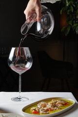 man pouring red wine into glass from decanter