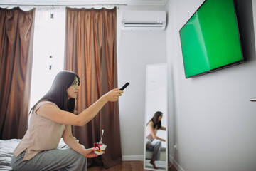 The girl is eating ice cream on the bed in front of the TV.