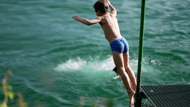 Boy jumping into lake water during hot summer day. Child diving in fresh lake splashing in super slow motion. Vacations concept