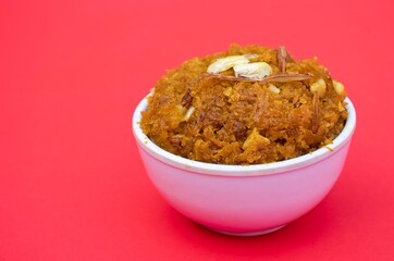 Homemade  Gajar Hawla or Carrot Halwa Garnished Almond and Cashew Nut in a White Bowl Isolated on Red Background with Copy Space for Texts Writing, Indian Sweets Desserts