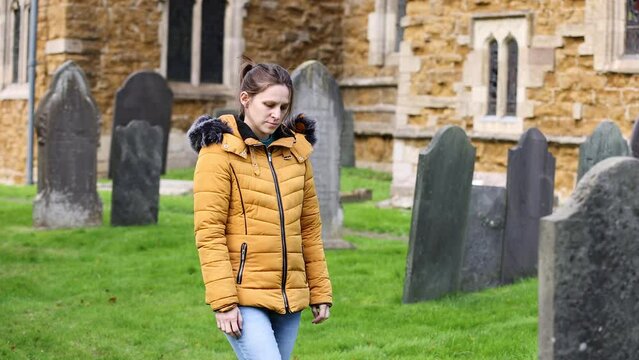 Young girl walking slowly and paying respects at a grave in church cemetery