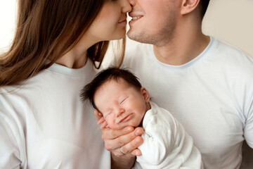 Close up portrait of young parents and newborn baby. Father and mother kiss and hug a beautiful newborn daughter. The concept of love, happy fatherhood and motherhood. Photography on white background.