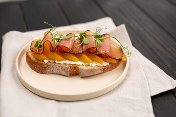 Toast on fresh bread with cream cheese, prosciutto and peach, decorated with micro greenery