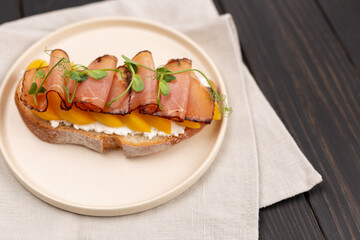 Toast on fresh bread with cream cheese, prosciutto and peach, decorated with micro greenery