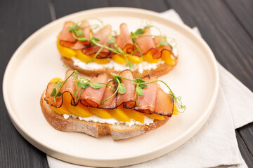 Toast on fresh bread with cream cheese, prosciutto and peach, decorated with micro greenery