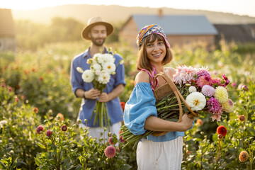 Portrait of cheerful man and woman stand as farmers with buckets full of freshly picked up dahlias...