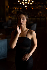 A young attractive woman in a black dress holds her hands near her face. Mysterious woman in thought.