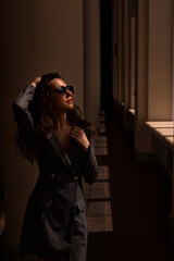 portrait of a woman.  A young attractive woman in sunglasses stands by a pillar of a building and looks out the sunny window.