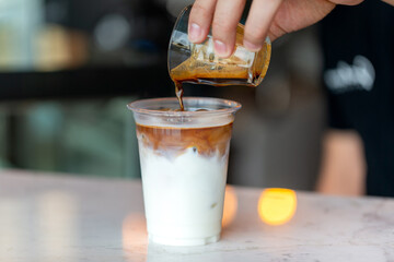 Barista preparing ice latte, pouring coffee into plastic cup with milk