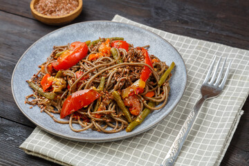 Soba with vegetables in soy sauce and teriyaki in a plate on a wooden table.