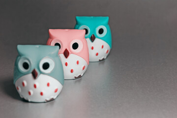 Close-up - three toy owls: green, gray and pink with white bellies, orange feathers and brown beaks.