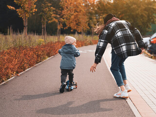 Mother help her son ride with kick scooter. Happy family mother teaches child son to ride a scooter in the Park. Support childhood parenthood idea. happy family concept