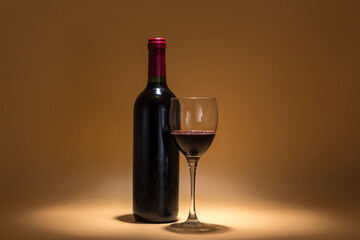 red wine bottle and wine glass, placed on a warm brown background