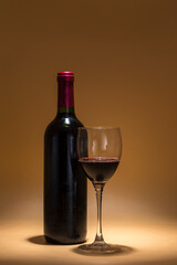 red wine bottle and wine glass, placed on a warm brown background