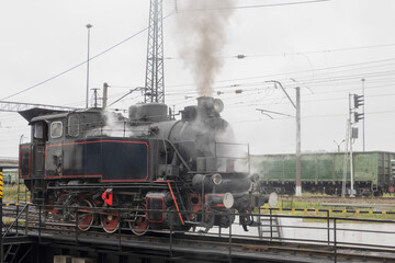 Fototapeta na wymiar a small steam locomotive, on a turning circle, blowing clouds of smoke at a railway station