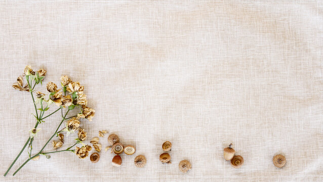 Fall banner of small dried roses and acorns; bottom border over a rustic woven cloth background