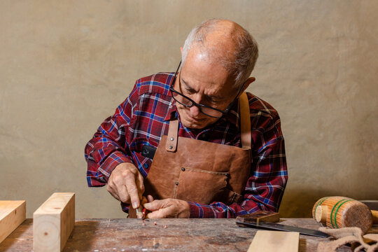 Latino older man carpenter by trade starting work sharpening his pencil with a chisel