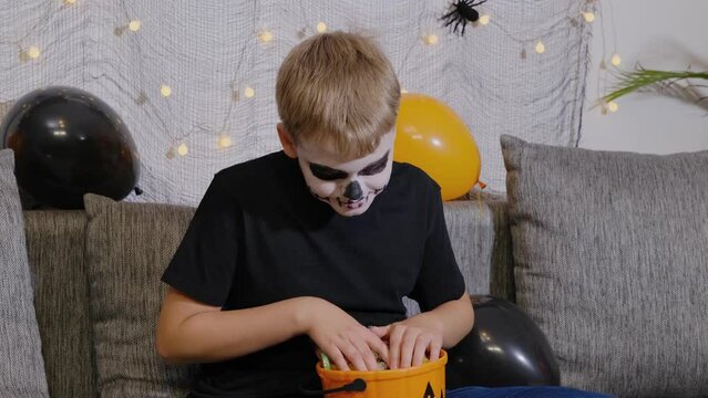 A boy in skeleton makeup pulls out candy from a Halloween party. Festive season in October.
