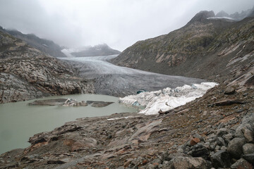 Scenic view on Rhone Glacier in swiss Alps with the lake. Rainy weather. High mountains landscape, arid terrain of Rhonegletscher, mountain trail in Switzerland.
