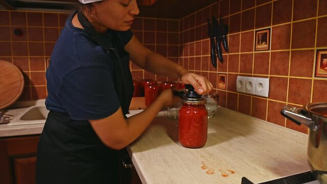 Side portrait of housewife closing lid on the jars with canned freshly boiled tomato juice or passata, with a seamer or special seaming key. Canning. Pickling. Cooking homemade tinned food. Marinating
