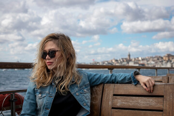 Young beautiful blonde tourist girl traveling on the ferry deck with the Bosphorus view in the background.