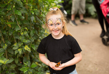 Young girl with butterfly face paint holding a beautiful orange butterfly.