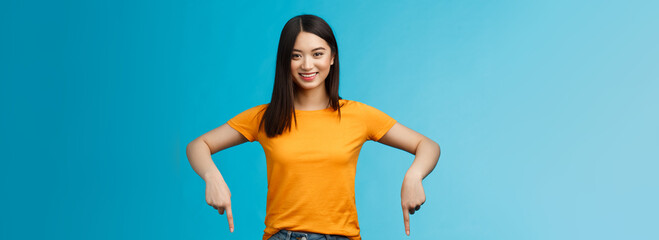 Cheerful self-assured asian girl dark haitcut wear yellow summer t-shirt introduce promo, pointing...